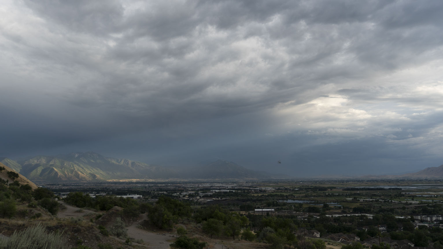 A break in the clouds sends light out to a far mountainside lighting its green slopes